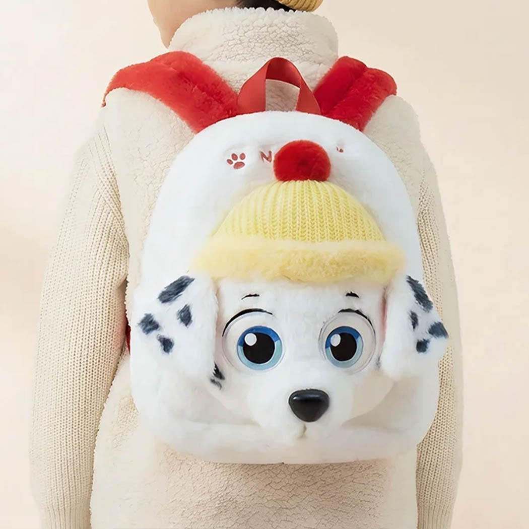 Un enfant portant sur son dos un sac à dos pat patrouille en peluche blanc, rouge et jaune.