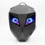 Un sac à dos LED moto extensible noir avec yeux programmables en forme de visage d’alien, avec une coque rigide noire et deux yeux lumineux bleus et roses sur fond blanc.