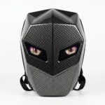 Un sac à dos LED programmable moto aspect fibre de carbone noir, avec une forme de casque et des yeux lumineux, posé sur fond blanc.