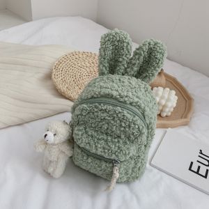 Zacht groen konijnenrugzakje met een wit bed, een boek en een teddybeer op de bodem